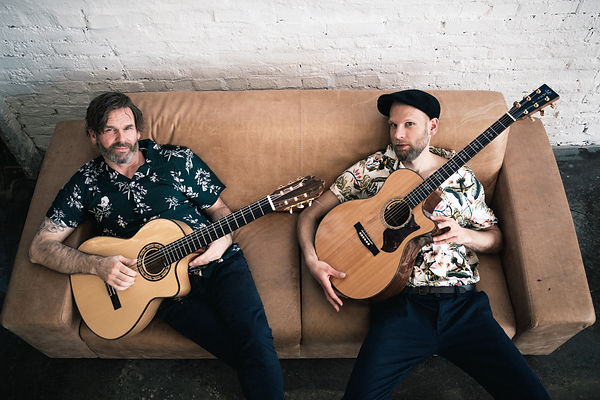 Gitarrenduo Barriola aus Düsseldorf liegt sitz auf Sofa, Gitarren in der Hand