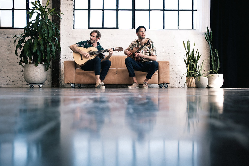 Zwei Gitarristen sitzen auf beigen Sofa mit Gitarre