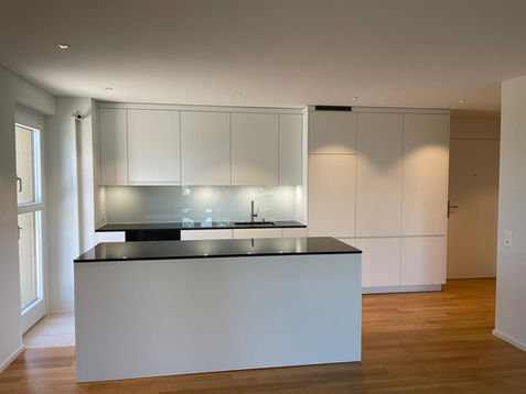 Weisse matte Küche von PBK DESIGN, 5610 Wohlen AG, mit Granit Carbon Black Arbeitsplatte und Glasrückwand, modernes und elegantes Küchendesign.