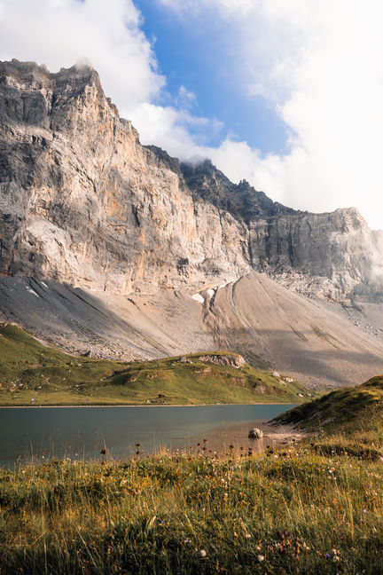 Blick auf den Seewlisee in der Schweiz, umgeben von majestätischen Bergen und grünen Wiesen, aufgenommen von Kyburz Visuals. Die Szene zeigt die beeindruckenden Felsformationen und das klare, ruhige Wasser des Sees unter einem teils bewölkten, teils sonnigen Himmel.