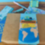A box with images of a suitcase, passport, map, travel ticket, compass, and a globe. Behind are puzzle cards.