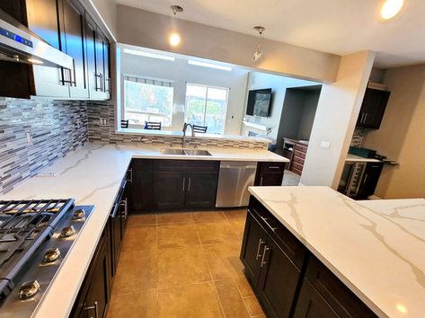 Spacious kitchen with a large center island, dark wood cabinets, and integrated modern appliances, under ambient lighting.