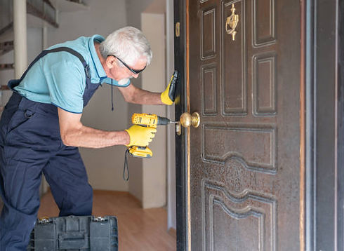 Senior technician using a power drill to install a door knob on a wooden door.