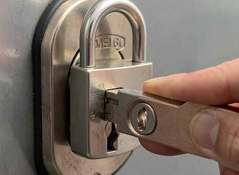 Hand inserting a key into a heavy-duty stainless steel padlock mounted on a grey metal surface
