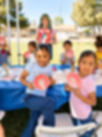 Smiling girls holding painted owl plates at an outdoor summer camp pottery activity