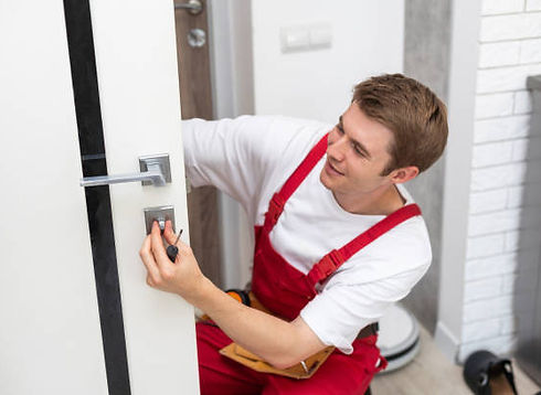 Smiling technician in red overalls installing a door handle lock with a screwdriver.
