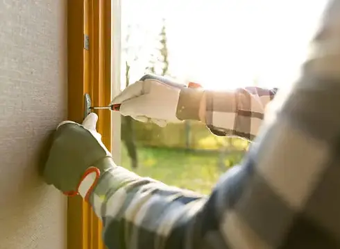 Gloved person using a screwdriver to fix a window frame fitting indoors.