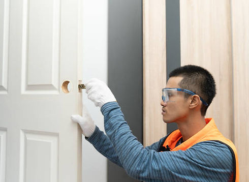 Worker in safety glasses and gloves installing a door knob on a white door