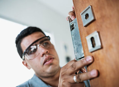 Technician with safety glasses fitting a lock mechanism into a wooden door.