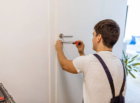 oung technician using a screwdriver to install a door handle on a white interior door.