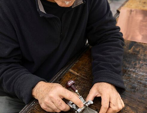 Elderly locksmith with glasses carefully cutting a key using a manual key cutter on a wooden workbench