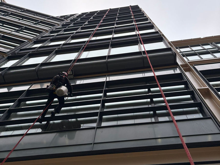 Rope access technician inspecting a dark glass facade