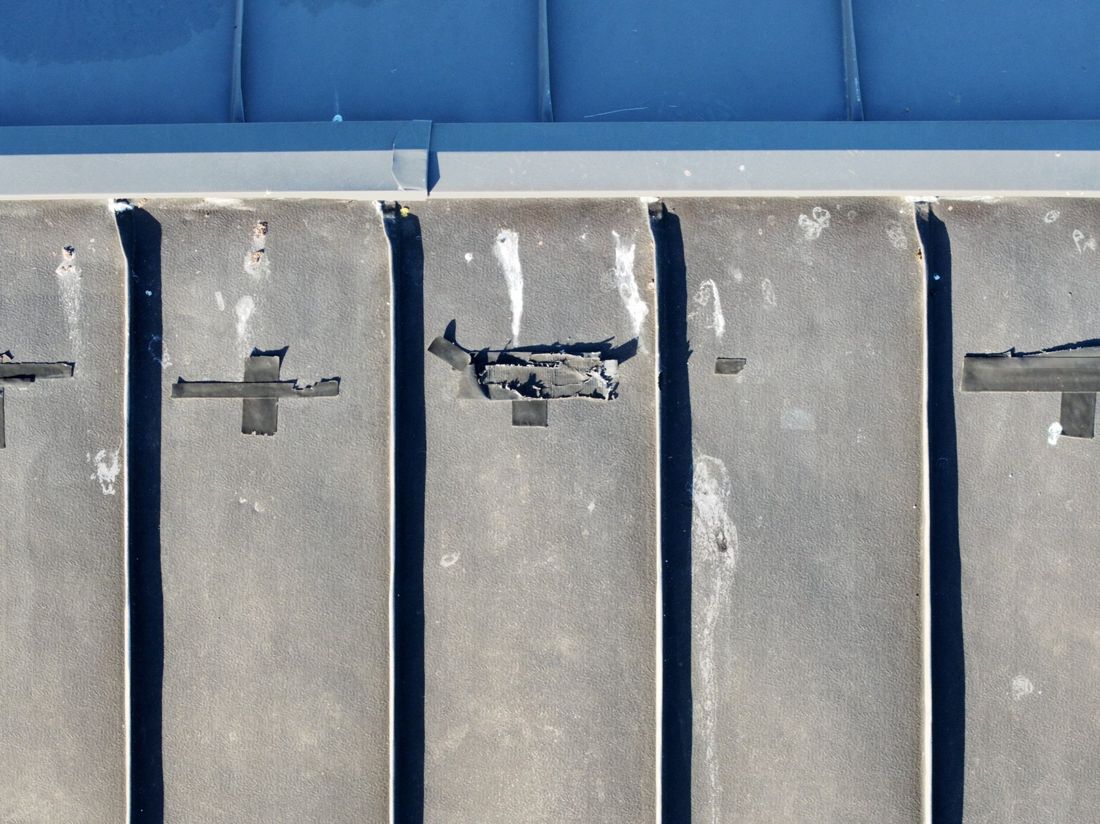 Drone close-up of tape patches split and lifting along membrane roof seams