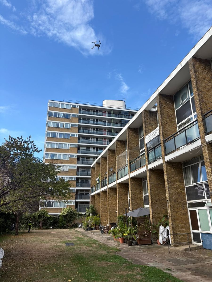 Survey drone flying beside a brick residential block and tower