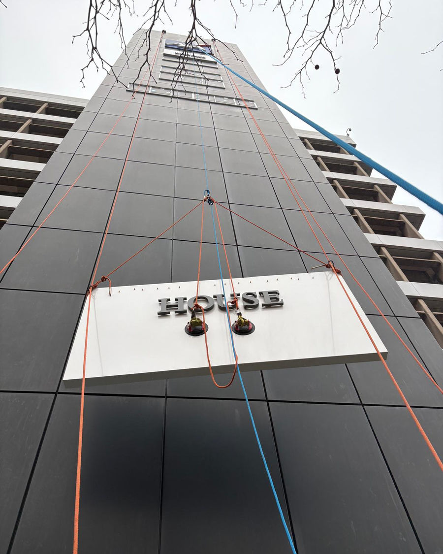Sign being hoisted up the cladding by powered winch
