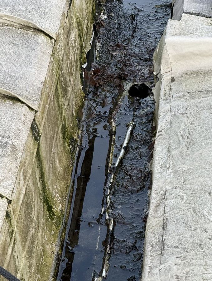 Box gutter holding standing water with silt at a blocked outlet