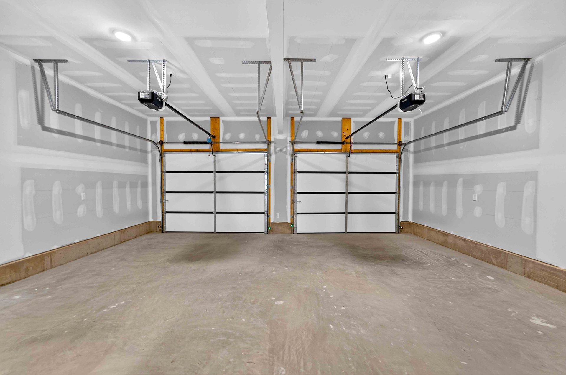Two-car garage in the Glenview new home design, featuring finished white walls, concrete flooring, and separate overhead garage doors.