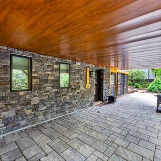 Covered outdoor patio with stamped concrete flooring, stone exterior walls, wood ceiling, recessed lighting, and sliding glass doors leading indoors.