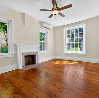 Renovated front living room featuring restored original hardwood flooring, preserved decorative fireplace surround, fresh neutral finishes, updated ceiling fan, abundant natural light, and carefully restored architectural details throughout this Stroudsburg home.