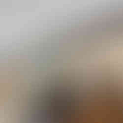 Interior view of an upper-level loft with dark hardwood flooring, exposed dark wood ceiling beams, and a modern railing with black metal posts and horizontal cable wires overlooking the living area below. Large black-trim windows fill the space with natural light, and a doorway leads to an adjoining room.