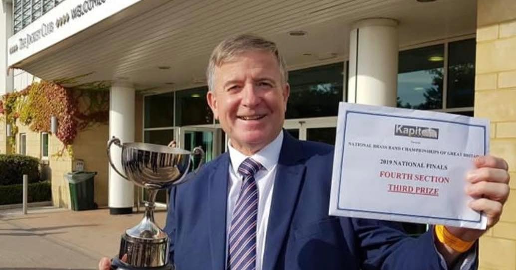 Keith Tywman holding a trophy and a third prize certificate from the 2019 National Brass Band Championships