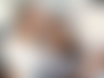 The photo shows a man in his mid-50s kissing a woman in her mid-30s on the forehead as they relax together on a couch, both smiling and wearing white shirts.