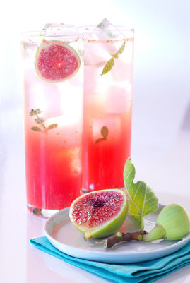 Pink cocktail with fig and mint garnish on a white surface with blue napkin.