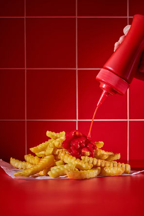 Arby’s crinkle-cut fries with ketchup being poured over them against a red tiled background.