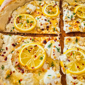 Pizza Bianca mit Zitronen, Kräutern, Nüssen und Chiliflocken auf Holzbrett, warm und appetitlich.