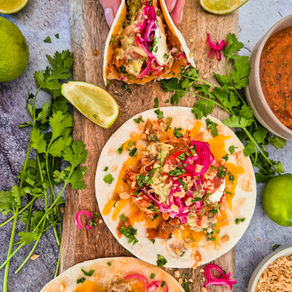 Tortilla mit Pulled Chicken, Avocado, roten Zwiebeln und Koriander auf Holzbrett, mit Limettenspalte.