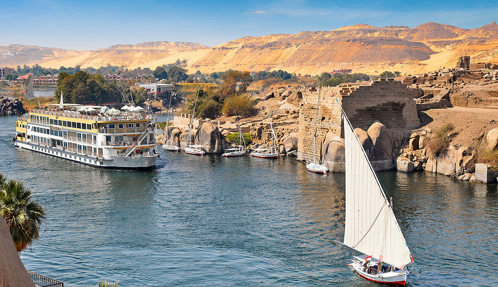 AmaDahlia river cruise ship and traditional sailboats on the Nile beside rocky riverbanks.