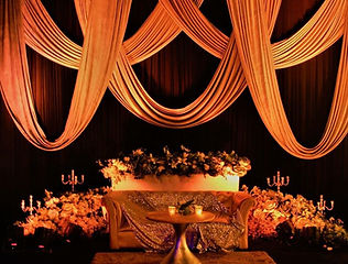 Draped reception stage with warm lighting by Kauvery Events