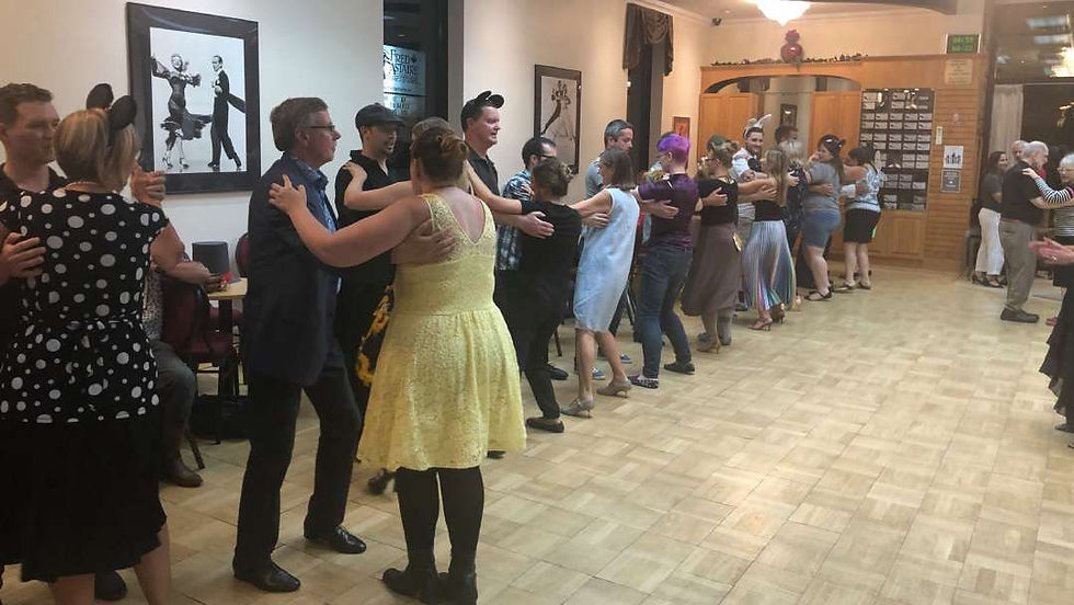 Adults dancing in pairs during a group class, moving energetically across a dance studio as part of a fun way to lose weight and stay active.