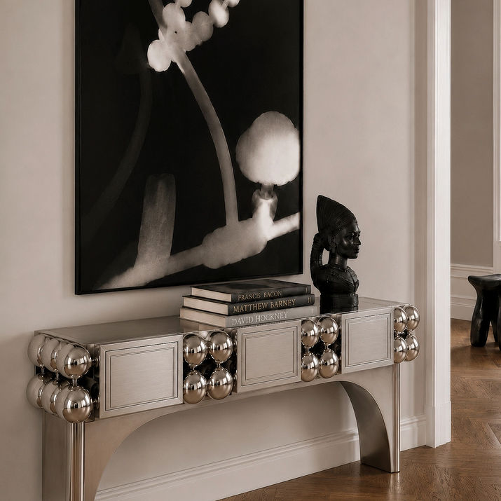 Orbital Console in polished steel with repeated spheres, framed relief panels and curved legs, shown in an interior setting.