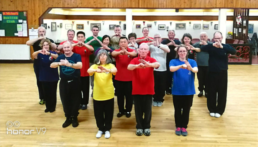 Grandmaster Zhu Chang Hai and his Monday Chen Style class in St. Michael`s Parish Centre in Belfast students of different age, nationality and gender with the hands in a position of greeting, left hand is opened, right hand is in a fist and they are connected in front of the body, chest height.
