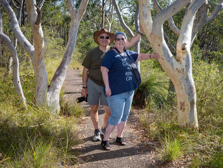 Smiling couple pose on a bush trail among white-barked trees; woman wears a blue Keep Calm and Kiwi On shirt.