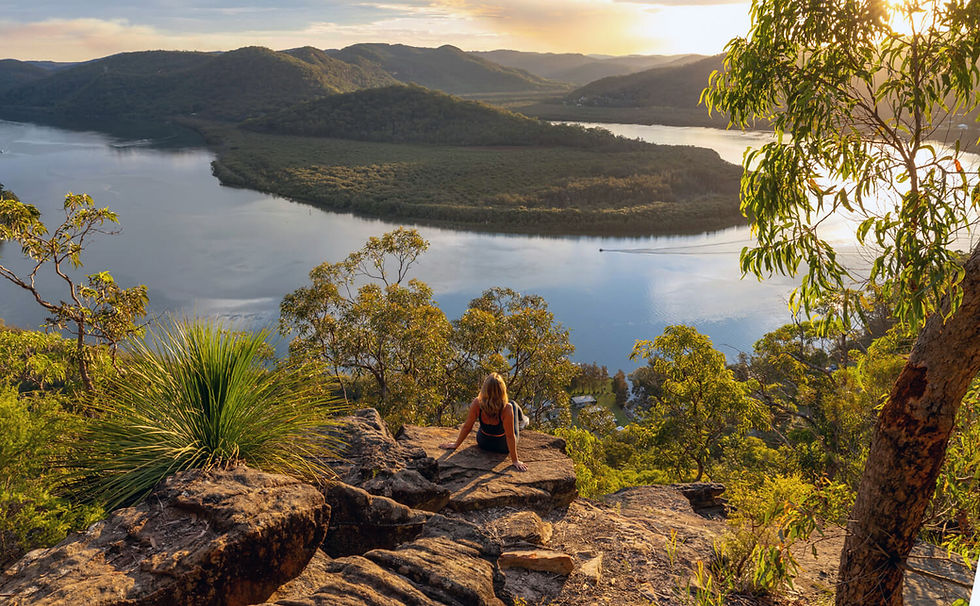 Person overlooking a wide river and forested hills at sunset