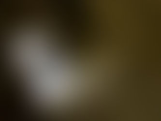 A person in a beige shirt and shorts explores a rugged cave, illuminated softly through an entrance, with rocky walls surrounding them.