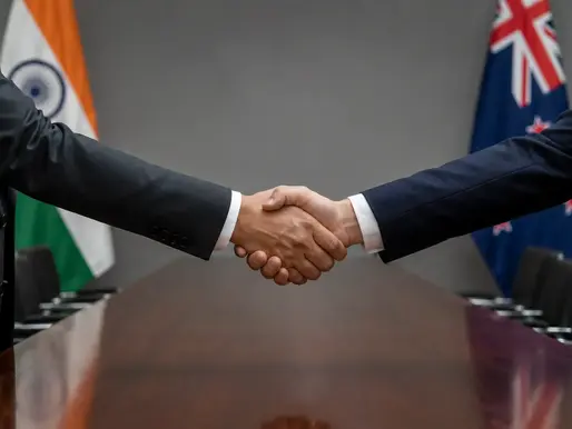 Two sets of hands in formal attire shaking hands across a conference table, representing the India-New Zealand Free Trade Agreement signed April 27, 2026