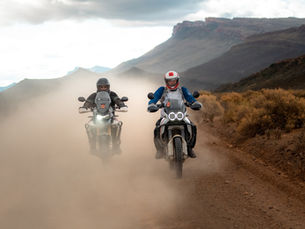 Two adventure motorcycle riders kicking up dust on a gravel road in South Africa’s Karoo landscape, showcasing the spirit of ADV riding.