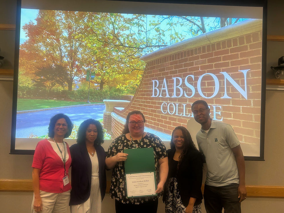 A group of five people standing together in front of a large screen displaying the Babson SUD Sprint Program Sign. The person in the center is holding a certificate, and the group is smiling