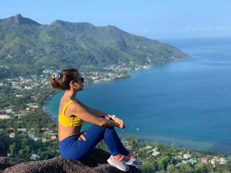 Woman sitting on a mountain cliff overlooking the ocean and coastal town in Seychelles.
