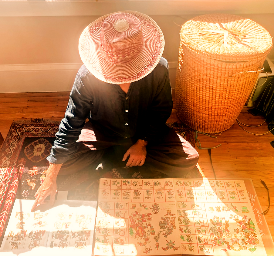 Person in a hat sits studying detailed documents of the Tonalpohualli on the floor.