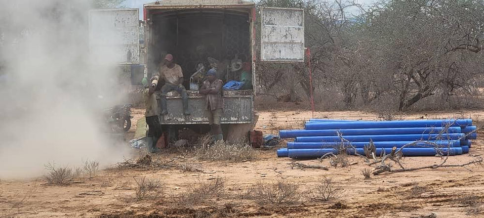 Männer sitzen in einem LKW, daneben blaue Rohre in dürrer Landschaft.