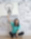 Junge Frau sitzt vor einer Wand mit Zeichnungen und hält ein Plakat mit einer Glühbirne – Symbol für Ideen und Kreativität bei Schule & Beruf Berlin e.V.
