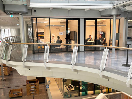 Innenansicht eines modernen, mehrstöckigen Gebäudes der IHK Berlin mit Blick auf verglaste Besprechungsräume, eine geschwungene Galerie und Treppenaufgänge.