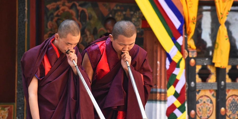 Mönche in traditionellen roten Gewändern spielen Trompeten auf dem Gelände eines Klosters.