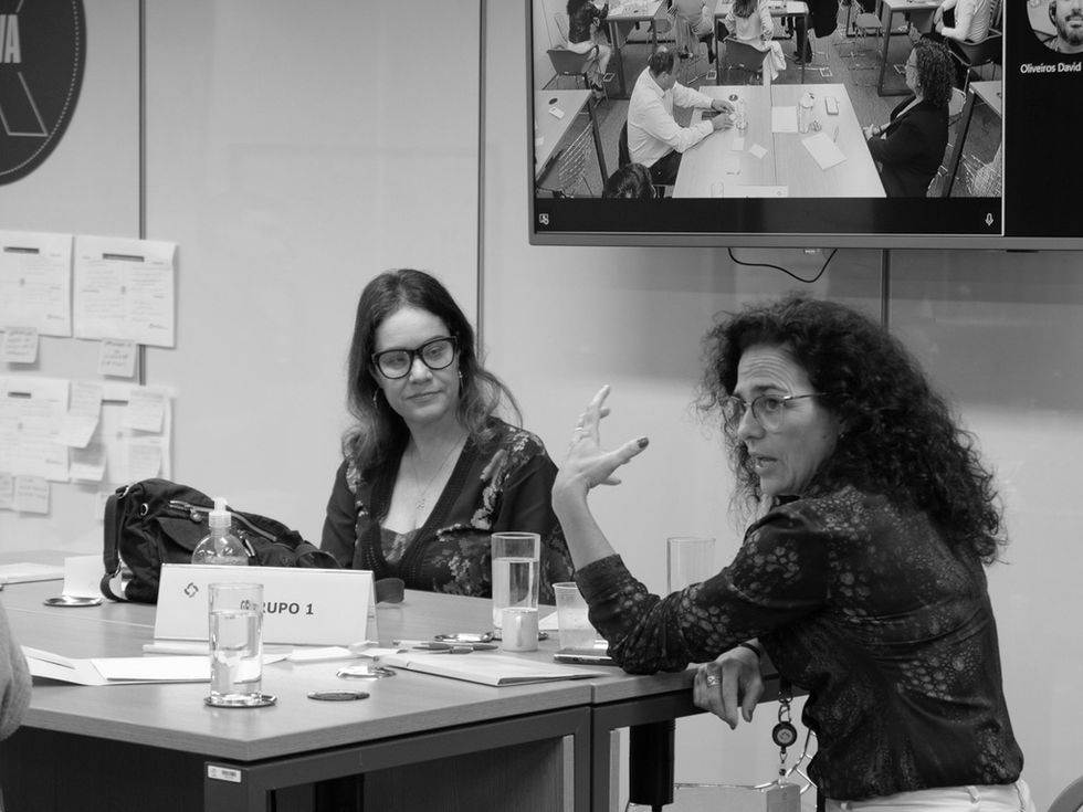 Participantes em oficina de inovação discutindo ideias em mesa de trabalho com post-its e materiais de apoio.