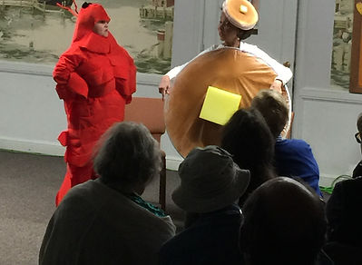 Lobster/Pancake cast photo of a person in a lobster costume talking to a person in a pancake costume.