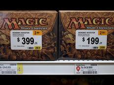 Trading card booster boxes with different price tags illustrating supply shortages and pricing challenges in the TCG market.